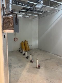 Empty room under construction with exposed pipes and ceiling grid.