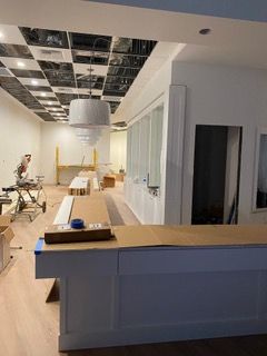 Interior under construction. White walls, wood floor, exposed ceiling grid, large light fixture.