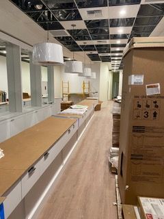 Interior retail space under construction, long counter with cardboard, unfinished ceiling, hanging lamps, and wood floor.