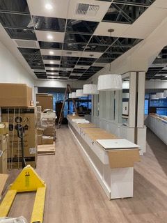 Interior of a store under construction with an exposed grid ceiling and long display counter. Boxes and equipment are present.