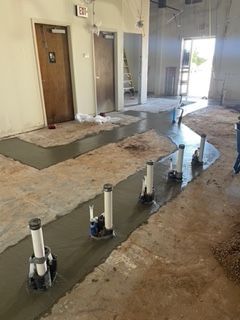 Concrete floor work in progress with several vertical pipe and pump structures. Doors visible in background.