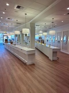 Empty jewelry store interior with white display cases, pendant lights, and wood-look flooring.