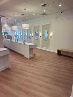 Empty retail store interior with wood-look flooring, white walls, and display cases, and decorative mirrors.