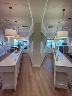 Interior of a store with long white countertops and hanging lamps, wooden floors, and windows.