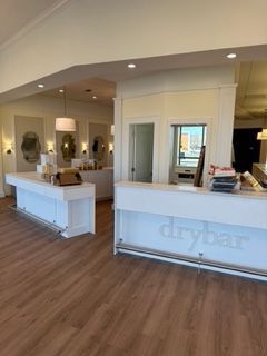Interior of a Drybar salon with white counters, wooden floors, and product displays.