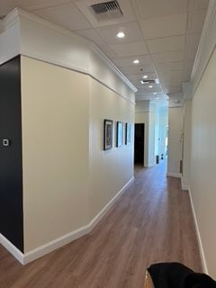 Narrow hallway with beige walls, brown flooring, and artwork.