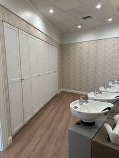 Salon interior: white cabinets, sinks, and wood-look flooring. Light-colored walls, recessed ceiling lights.