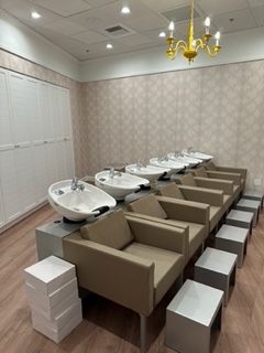 Salon with shampoo stations and beige chairs, footrests, and white sinks.