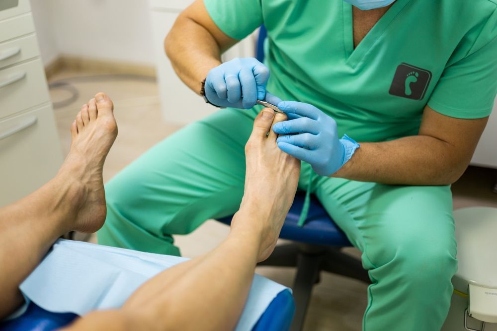 A person is getting their toenails trimmed by a doctor wearing green scrubs — Podiatrist in Forster, NSW