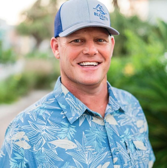 A man wearing a baseball cap and a blue shirt is smiling.