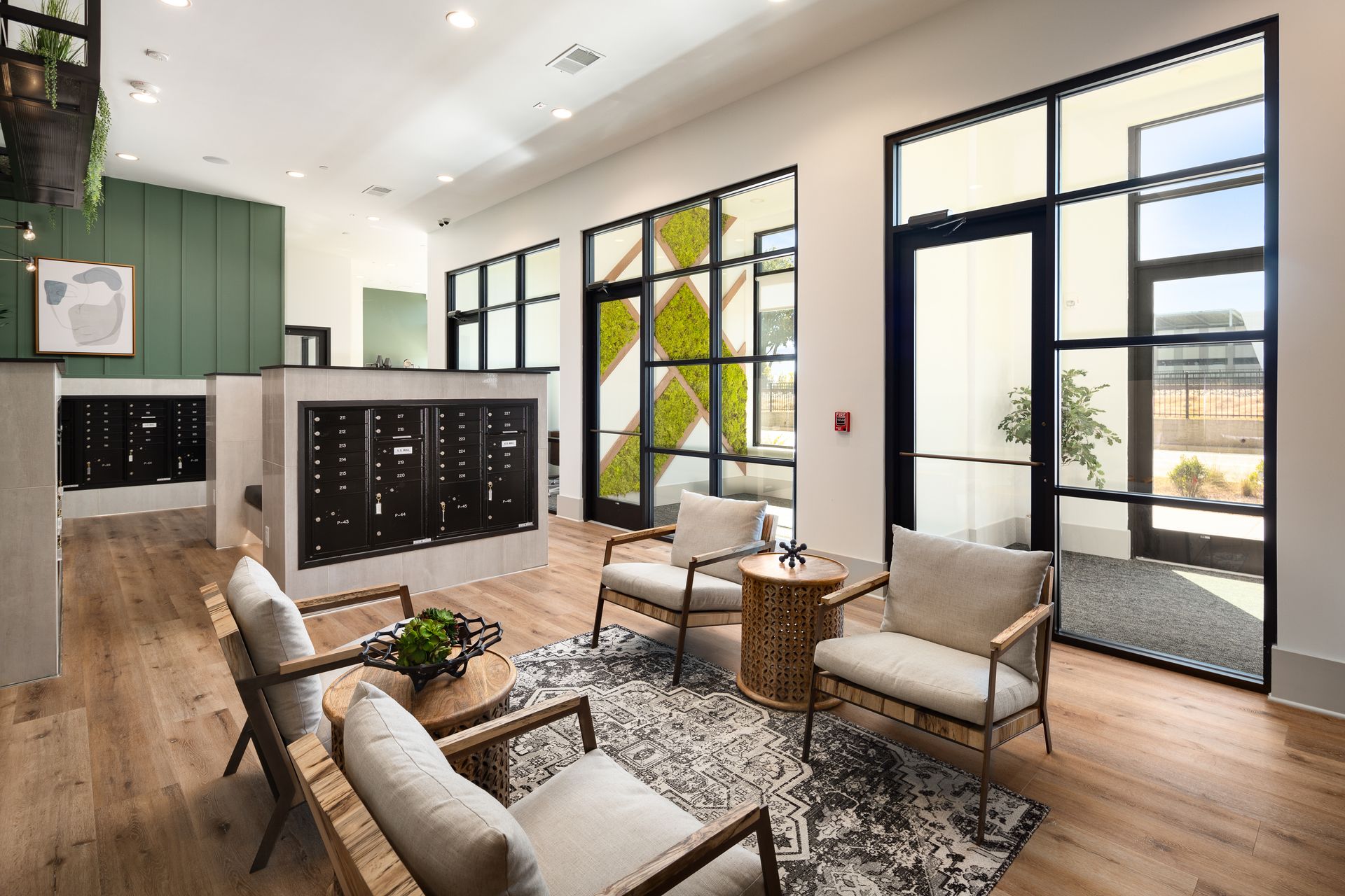 Modern lobby with tan chairs, patterned rug, wood floors, black lockers, and tall windows.