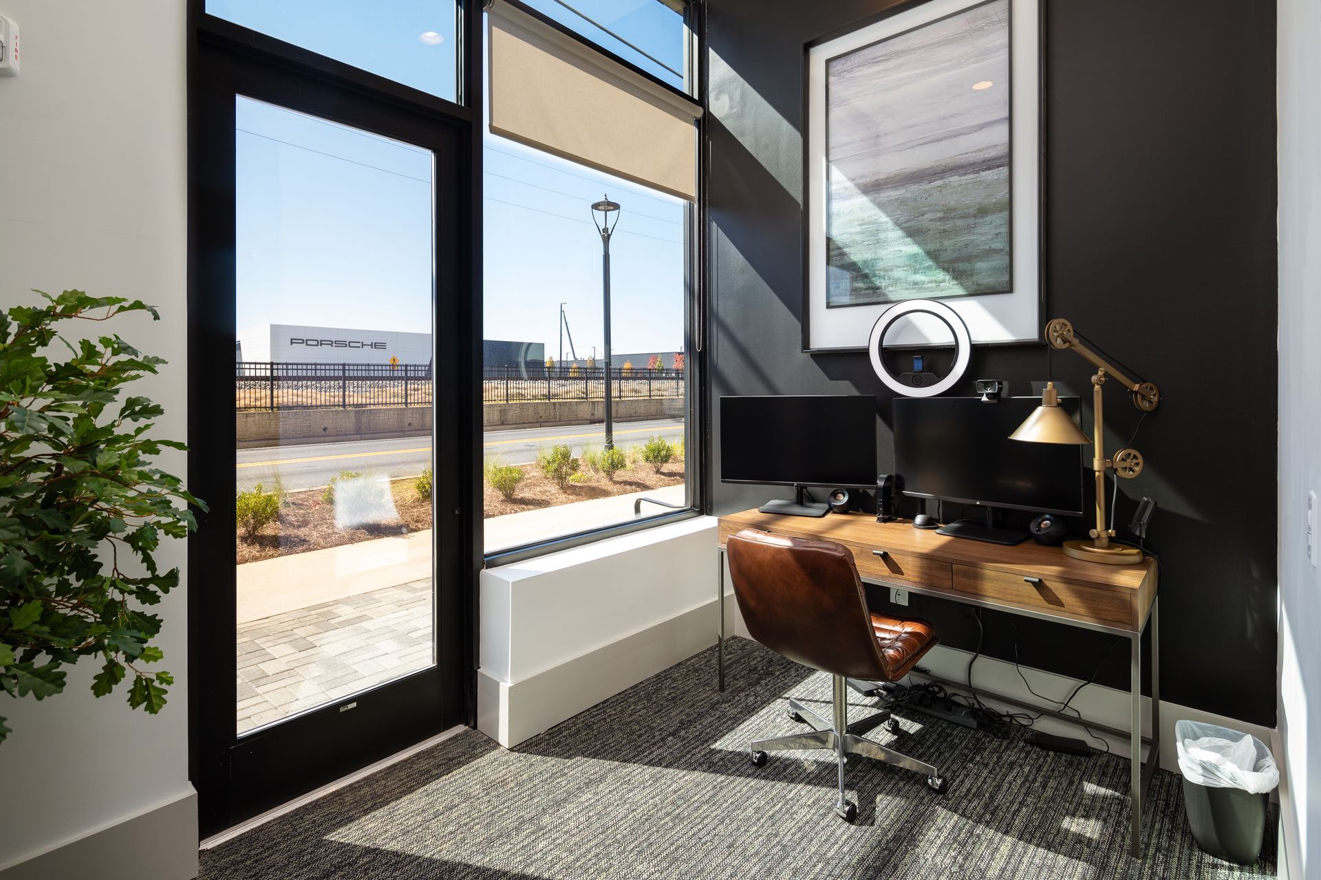 Modern office corner with desk, chair, lamp, and large windows overlooking an outdoor view