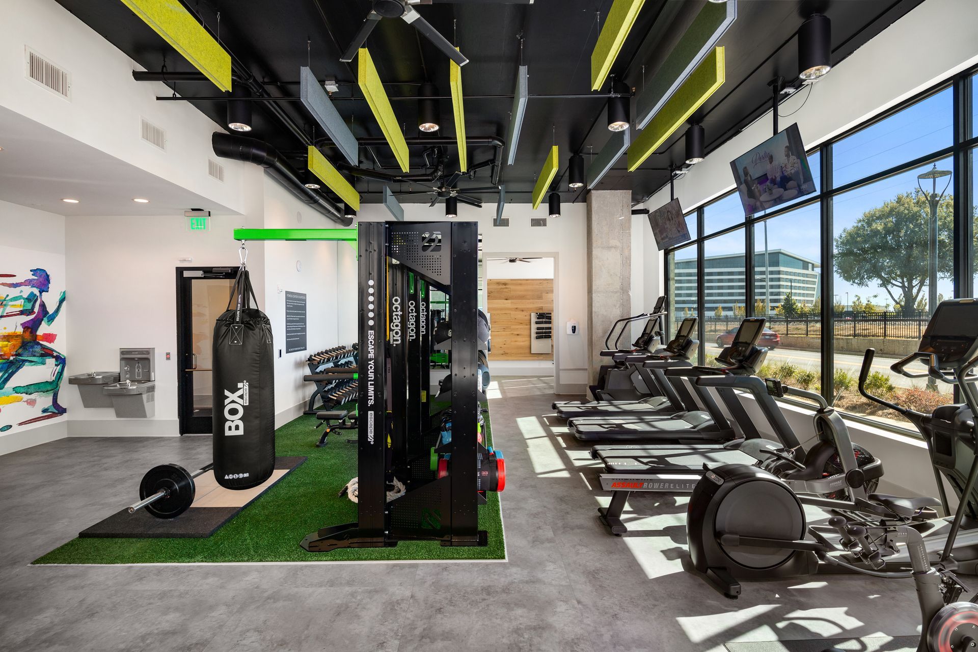 Modern gym with weight machines, rowing equipment, and treadmills beside large windows