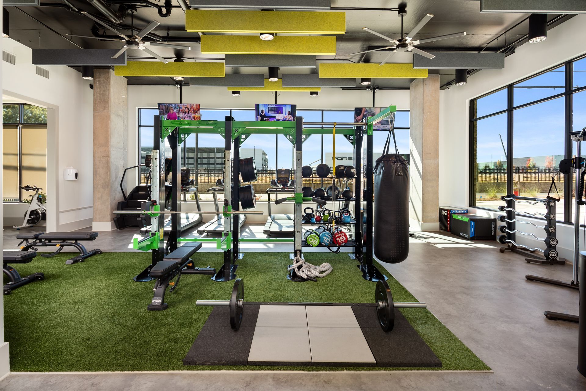 Modern gym with squat rack, pull-up bar, bench, and hanging punching bag on turf indoors
