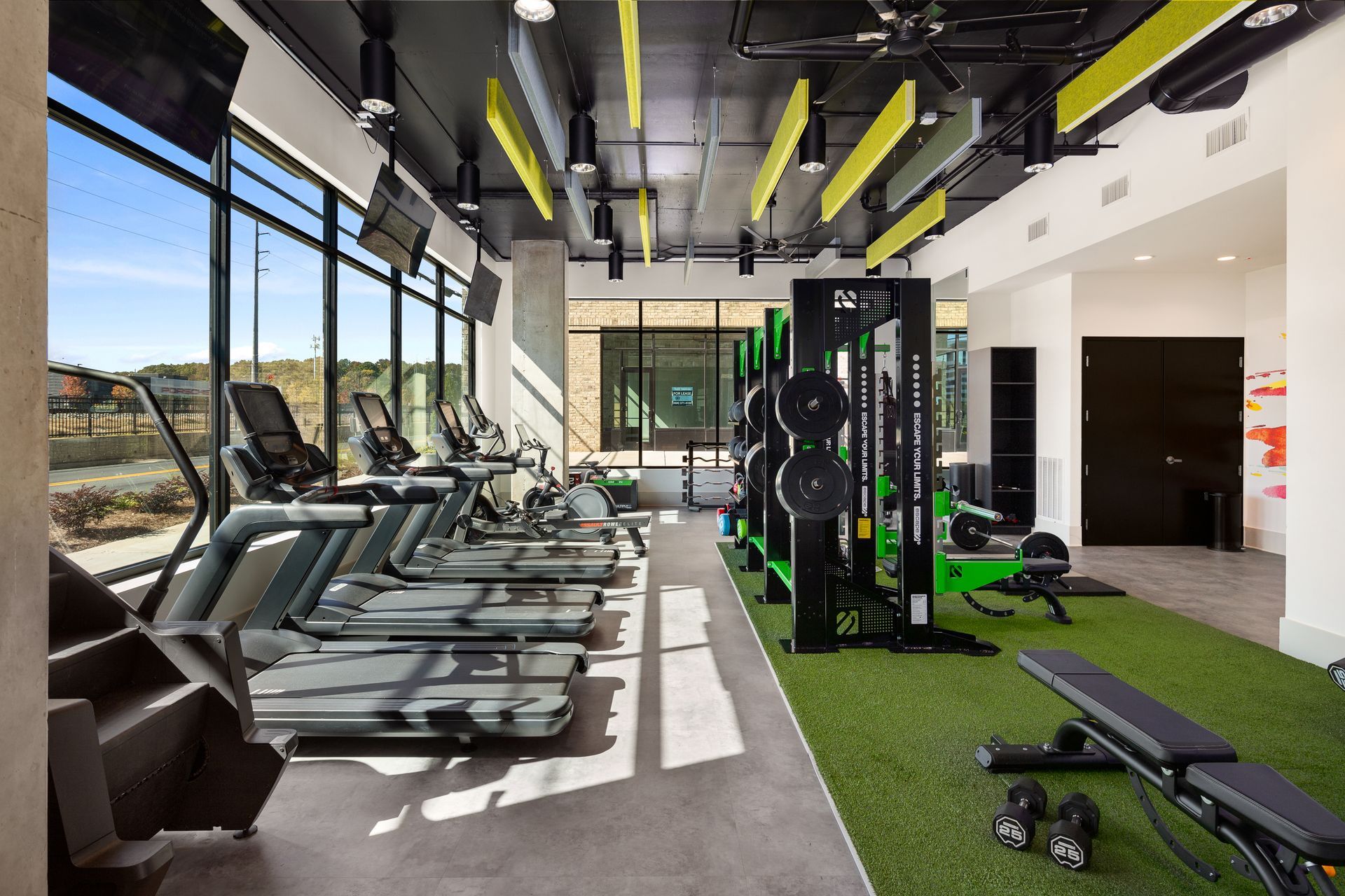 Modern gym interior with treadmills, weight machines, and green turf by large windows