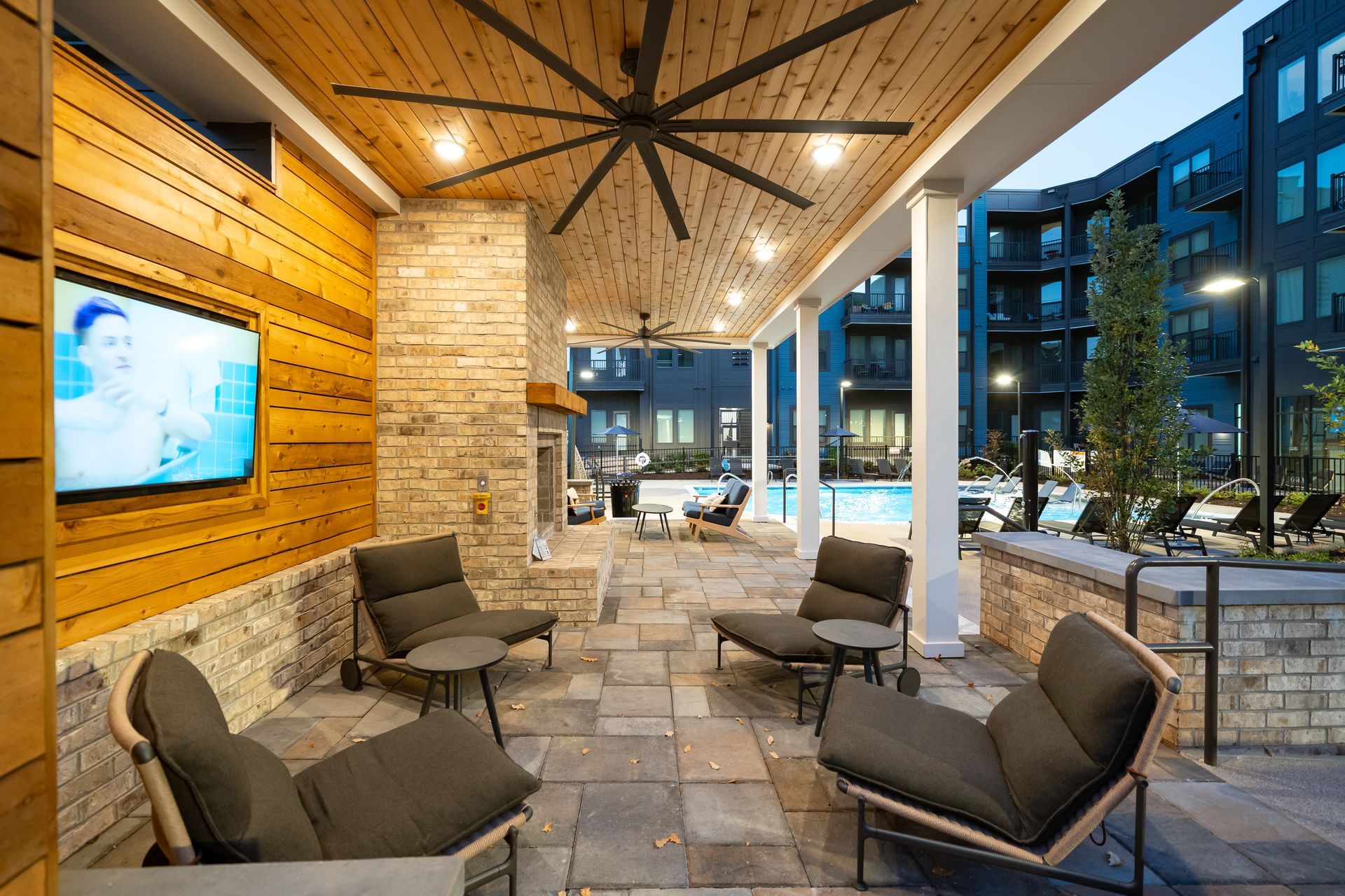 Modern outdoor lounge with cushioned chairs, stone floor, wood ceiling, and city lights at night