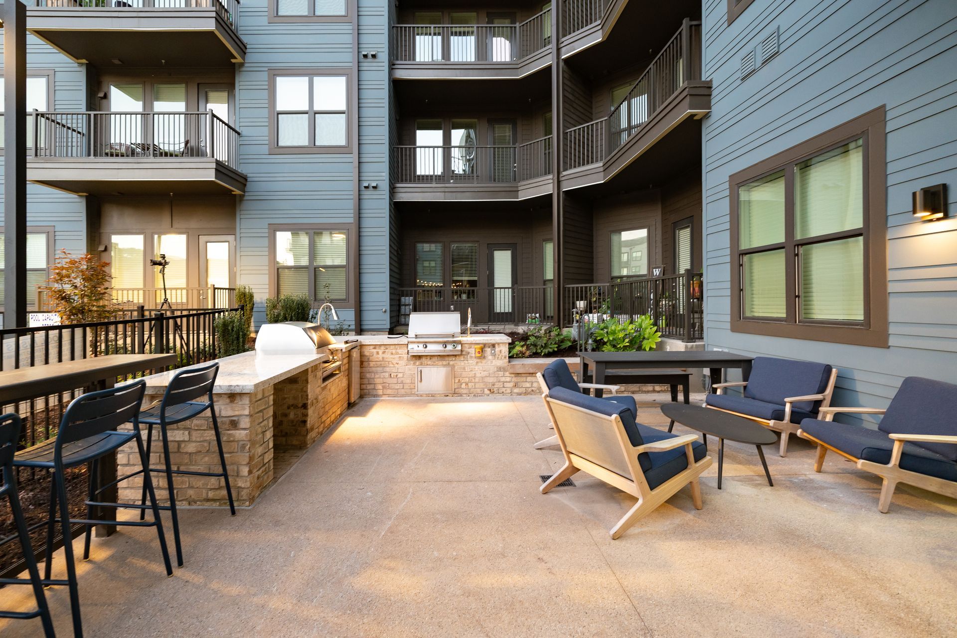 Apartment courtyard with patio seating, stone fire pit, and balconies around a modern building.
