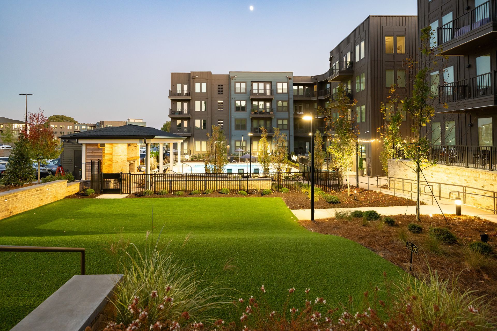Modern apartment complex with lit windows and landscaped green courtyard at dusk