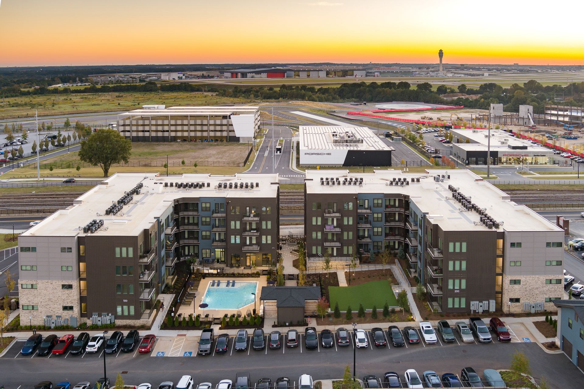 Aerial view of a modern apartment complex with a central pool and parking lot at sunset.