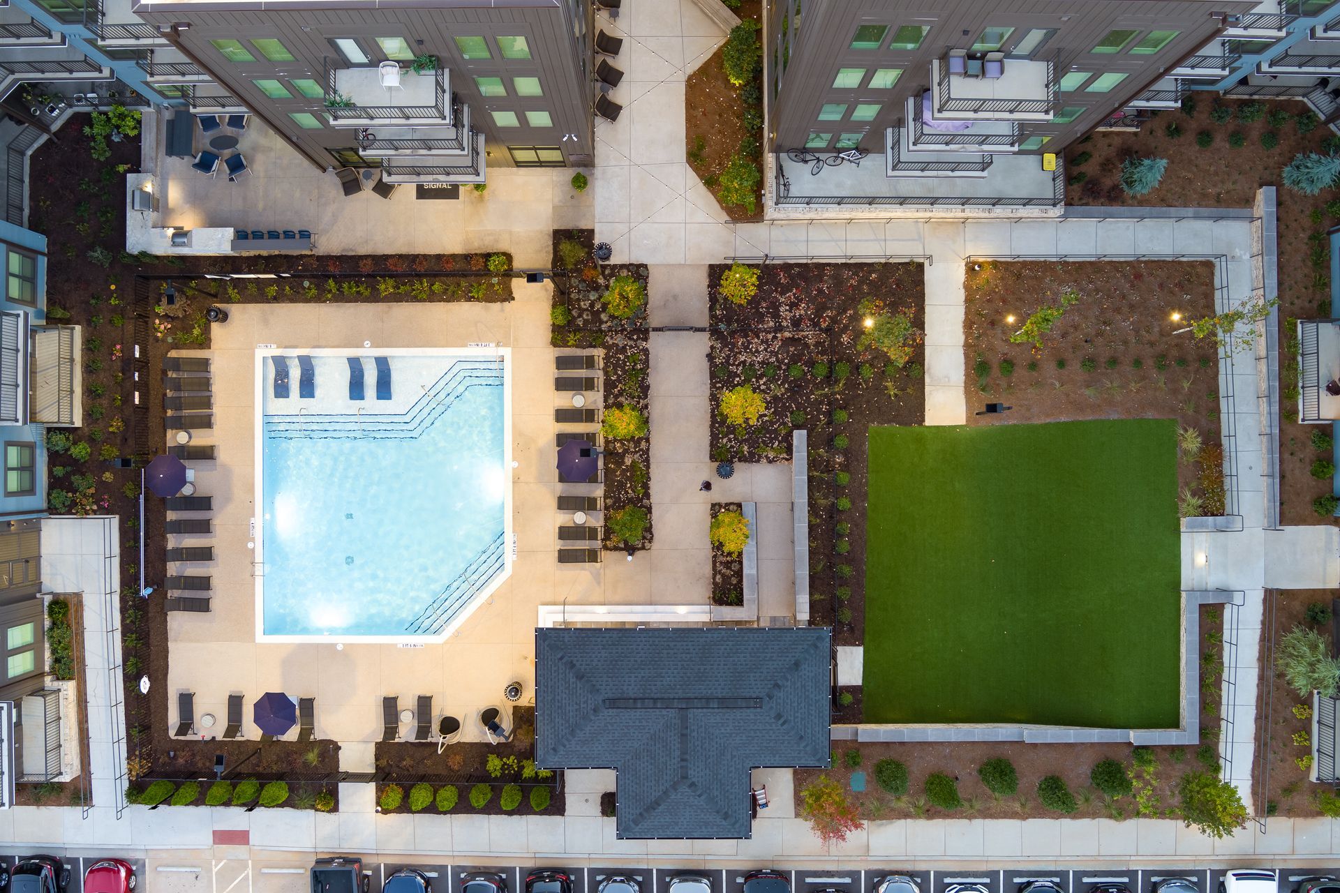 Overhead view of a courtyard with a swimming pool, green lawn, and surrounding apartment buildings