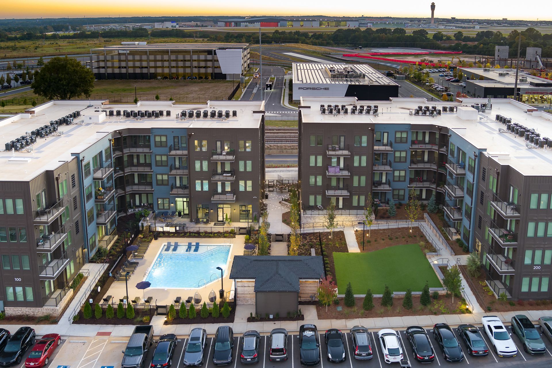Aerial view of modern apartment buildings around a central pool and courtyard with parked cars in front.