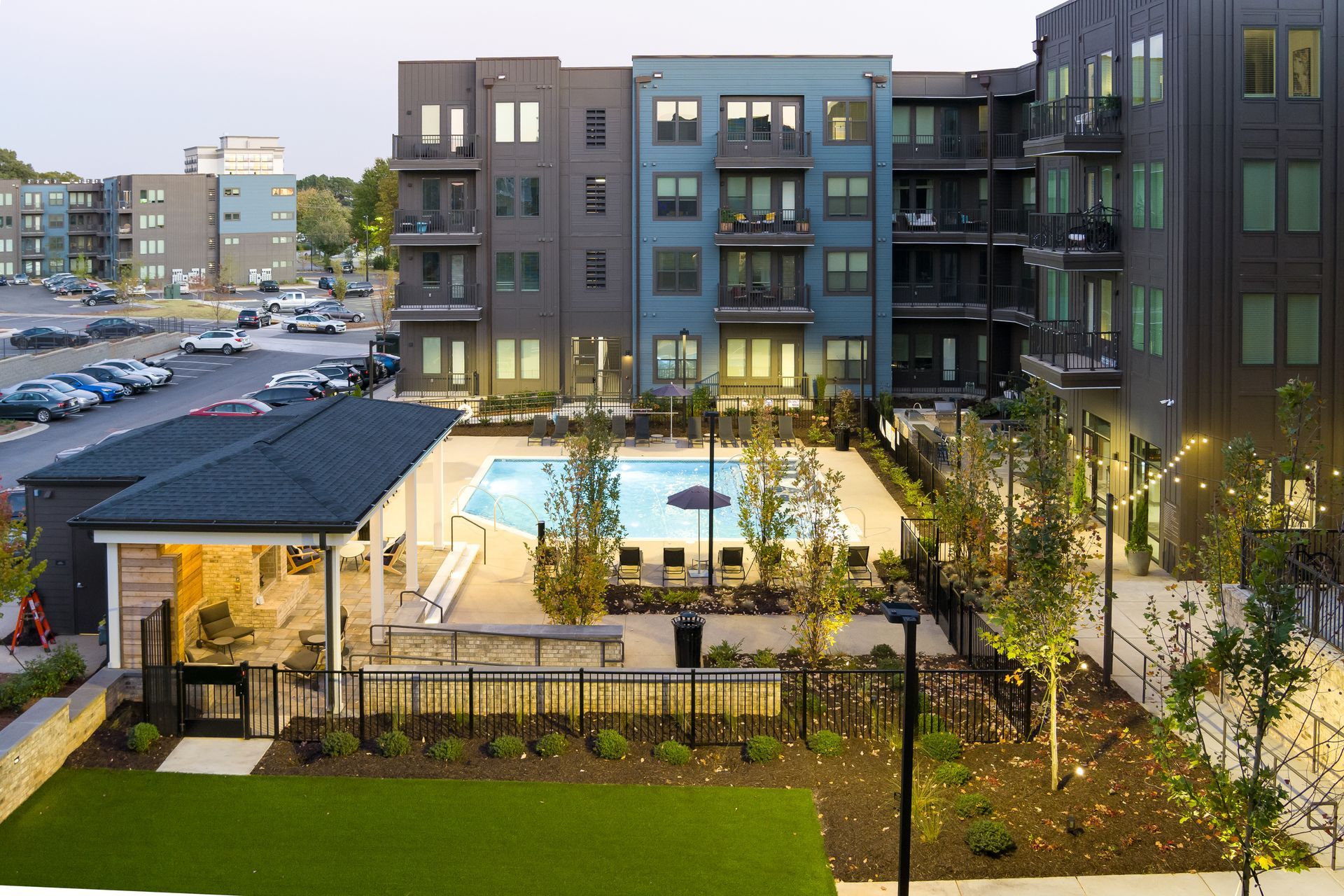 Apartment complex courtyard with a lit pool, patio seating, and landscaped greenery at dusk