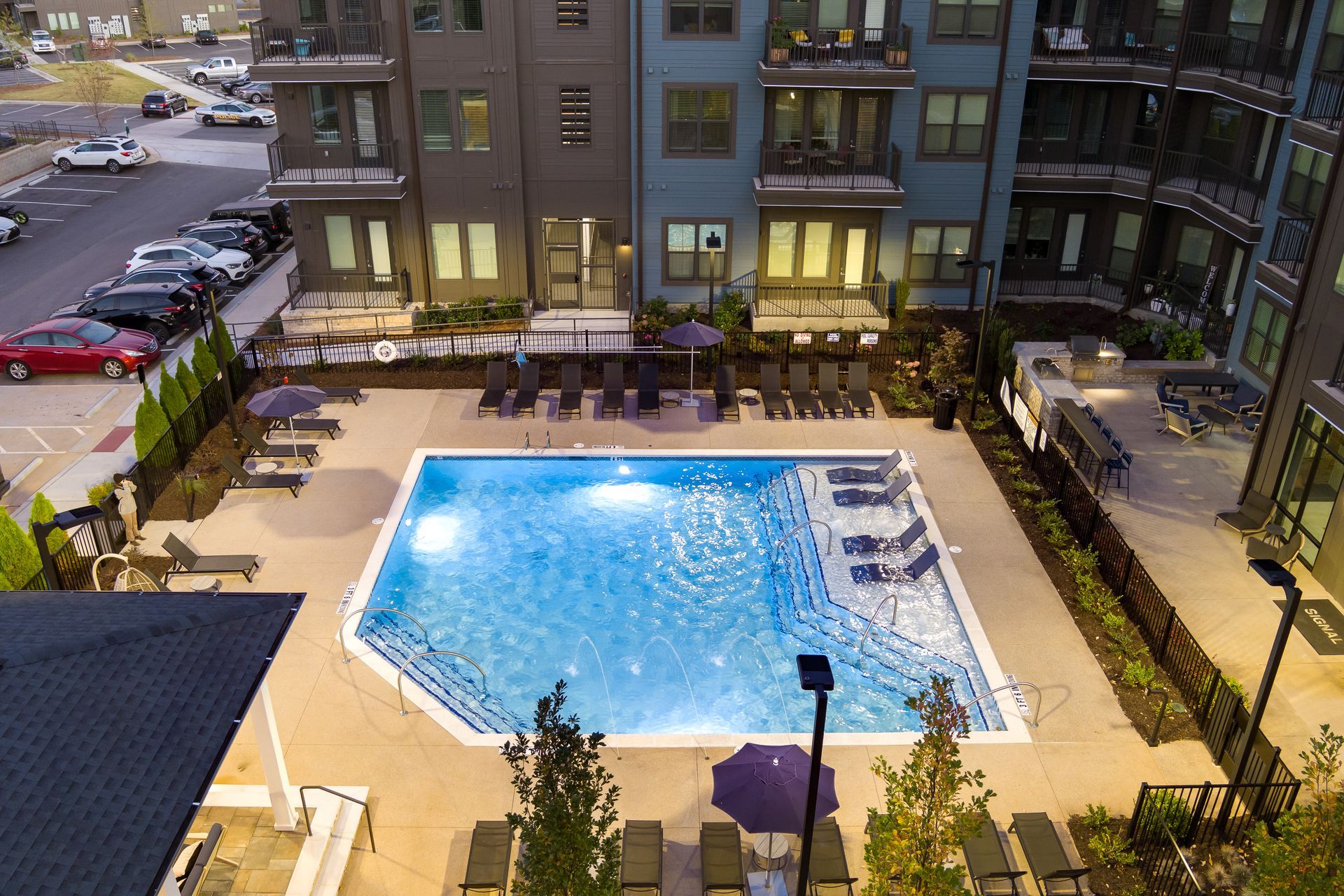 Courtyard pool with blue water surrounded by apartment buildings and lounge chairs at dusk
