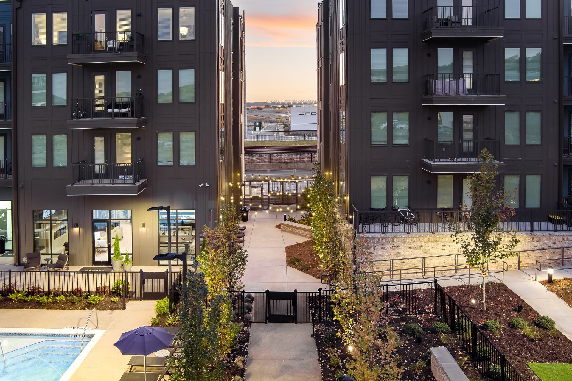 Modern apartment courtyard between two dark buildings at sunset, with lit windows and a central pathway.