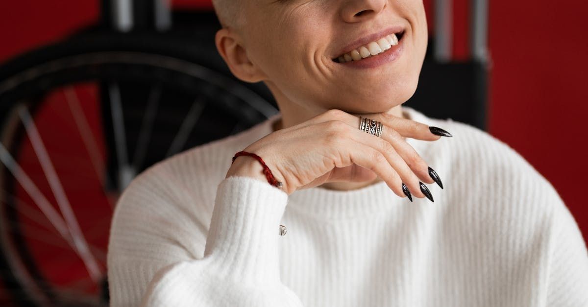 A woman with a bald head is wearing a white sweater and smiling.