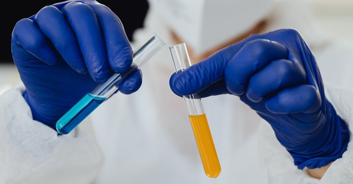 A person wearing blue gloves is holding a test tube with a yellow liquid in it.