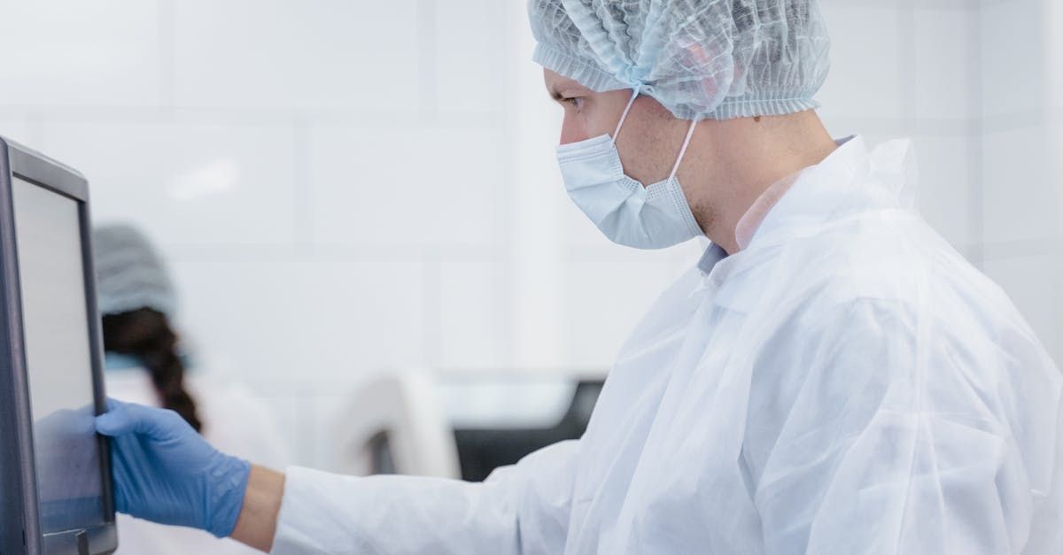 A scientist wearing a mask and gloves is using a computer in a laboratory.