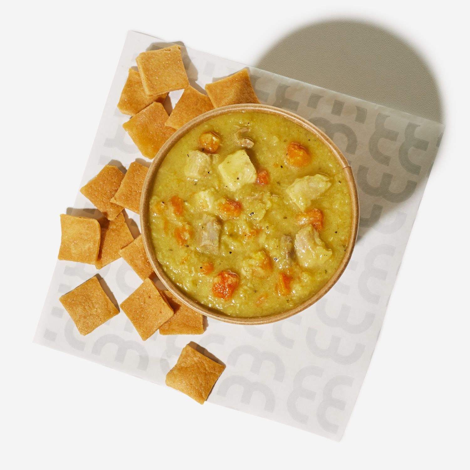 A bowl of soup is surrounded by croutons on a napkin