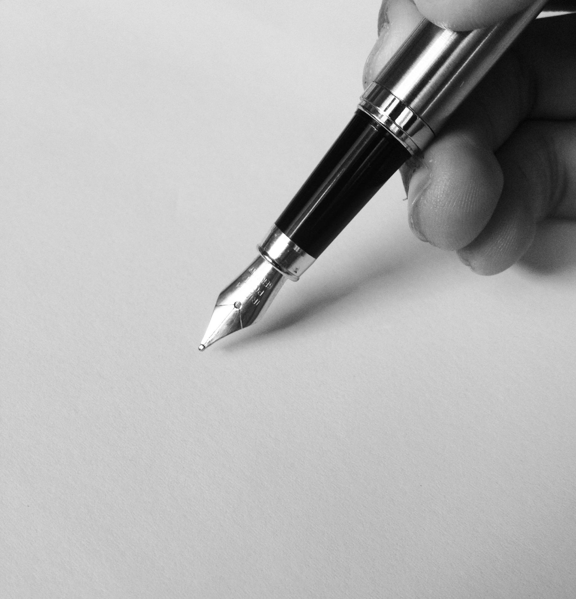 Hand holding a silver and black fountain pen poised over blank white paper.