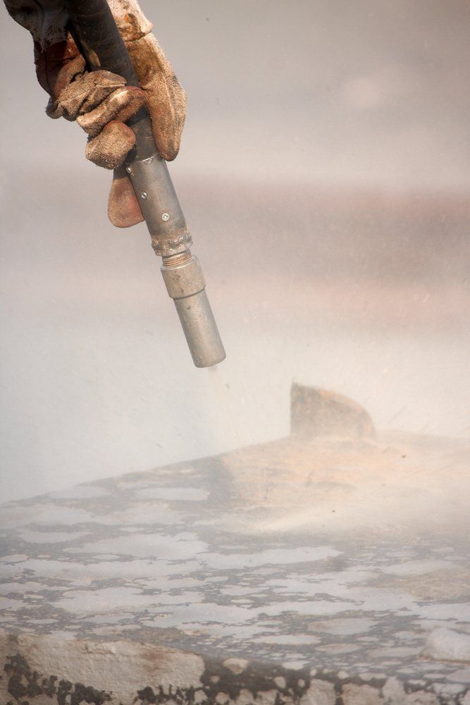 A person wearing gloves is holding a sand blaster over a concrete surface — Mayric Engineering in Forster, NSW