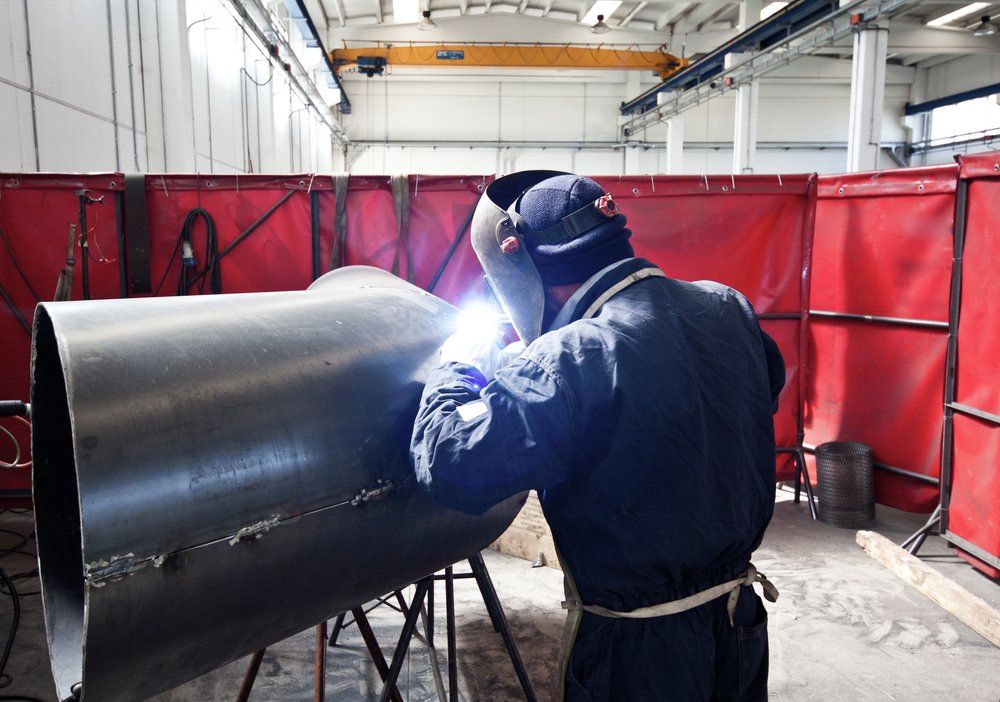 A Man Is Welding a Metal Pipe in A Factory — Mayric Engineering in Wingham, NSW