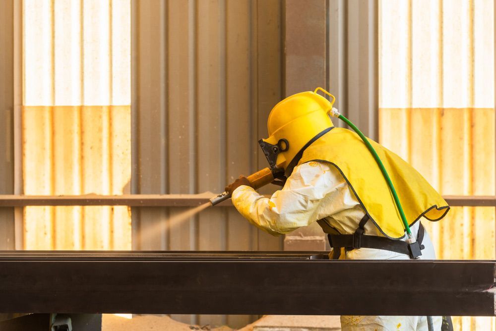Man in a Yellow Helmet is Sandblasting a Piece of Metal in a Factory — Mayric Engineering in Taree, NSW
