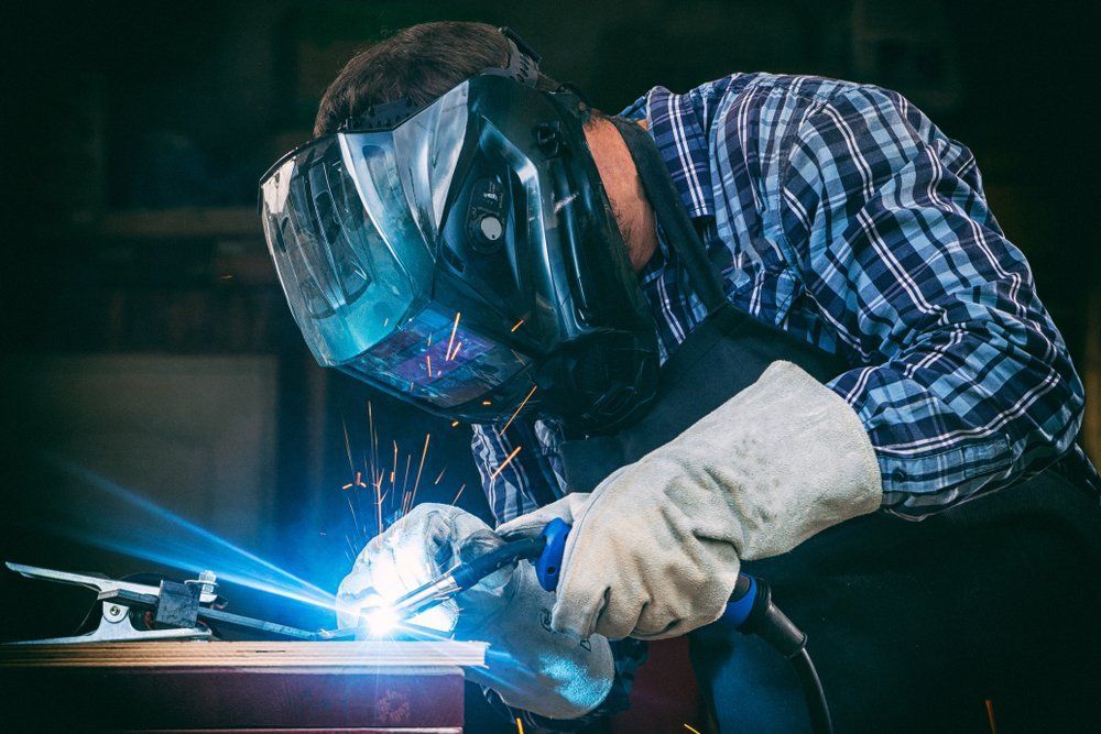 A Man Wearing a Welding Mask and Gloves Is Welding a Piece of Metal — Mayric Engineering in Hallidays Point, NSW