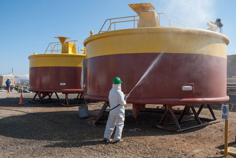 A Man in A Protective Suit Is Cleaning a Large Tank with A High Pressure Washer — Mayric Engineering in Taree, NSW