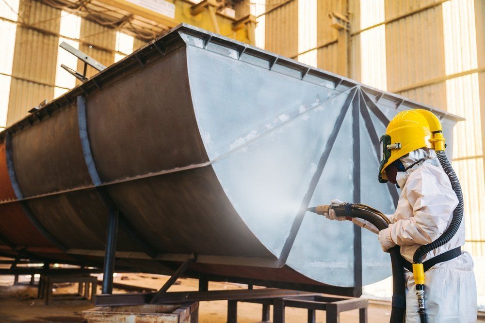 A Man Is Sandblasting a Large Piece of Metal in A Factory — Mayric Engineering in Forster, NSW