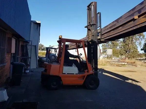 A Man Is Driving an Orange Forklift in A Parking Lot — Mayric Engineering in Wingham, NSW