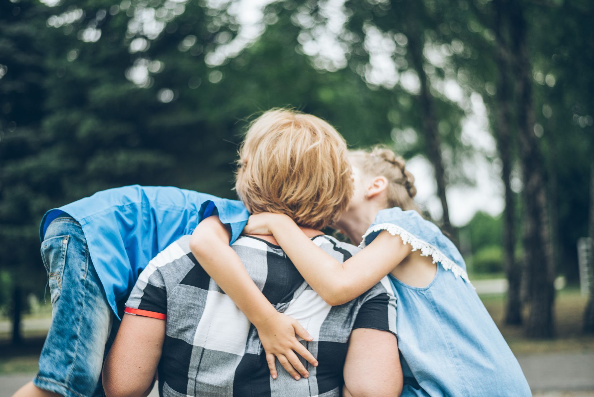 A man is carrying two children on his shoulders in a park.