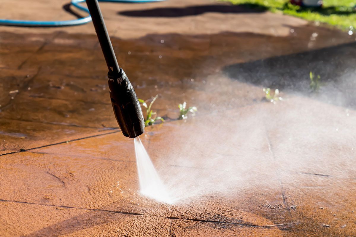 A person is using a high pressure washer to clean a patio.