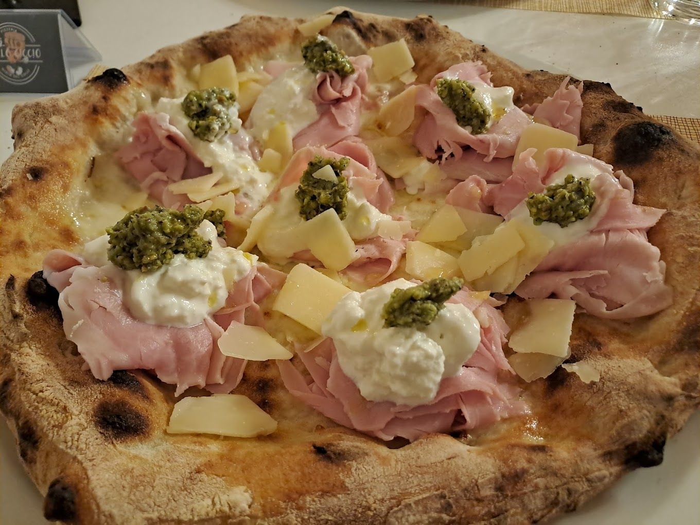 Una pizza con prosciutto e formaggio è su un piatto bianco.