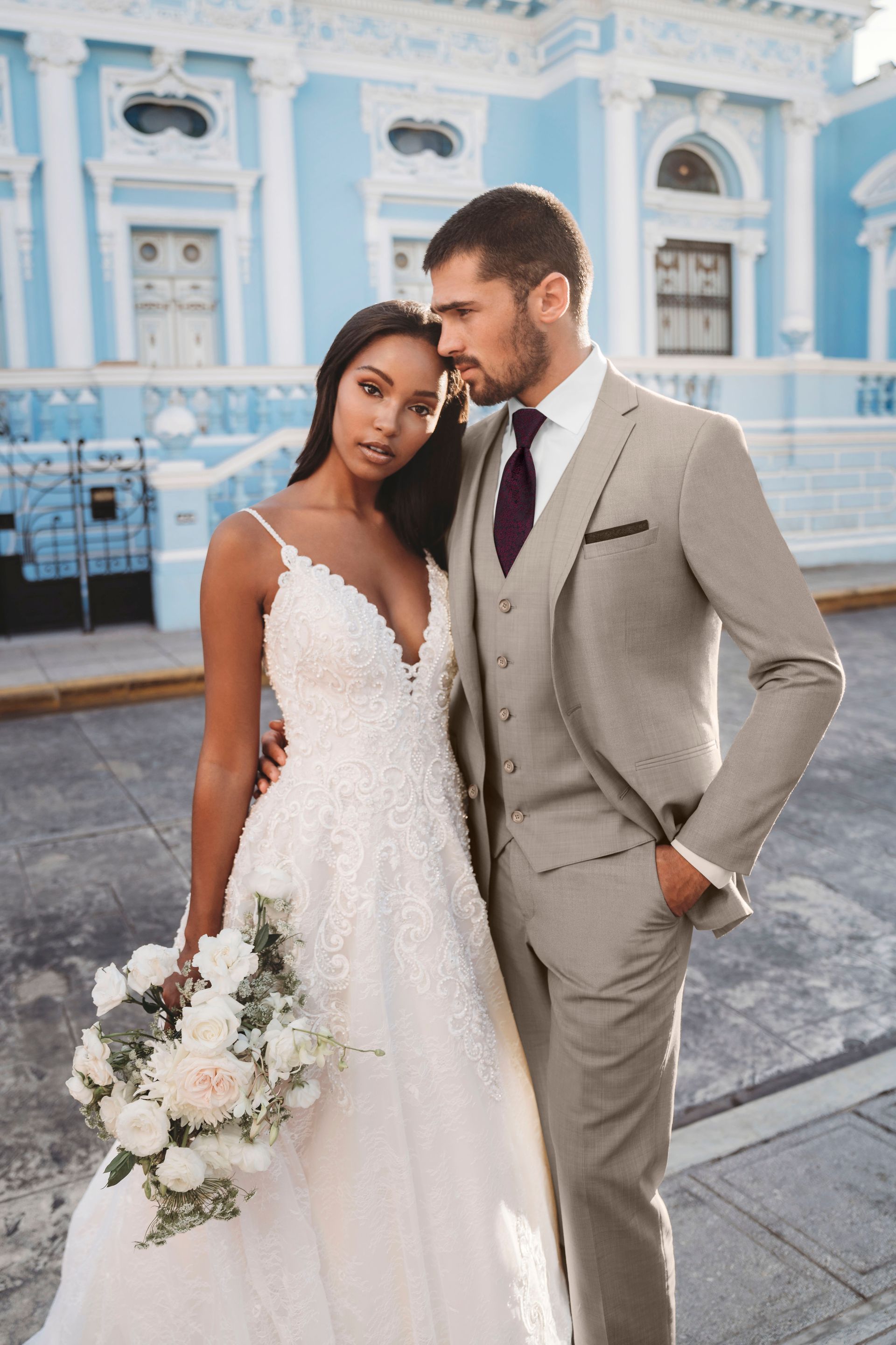 A bride and groom are posing for a picture in front of a blue building.