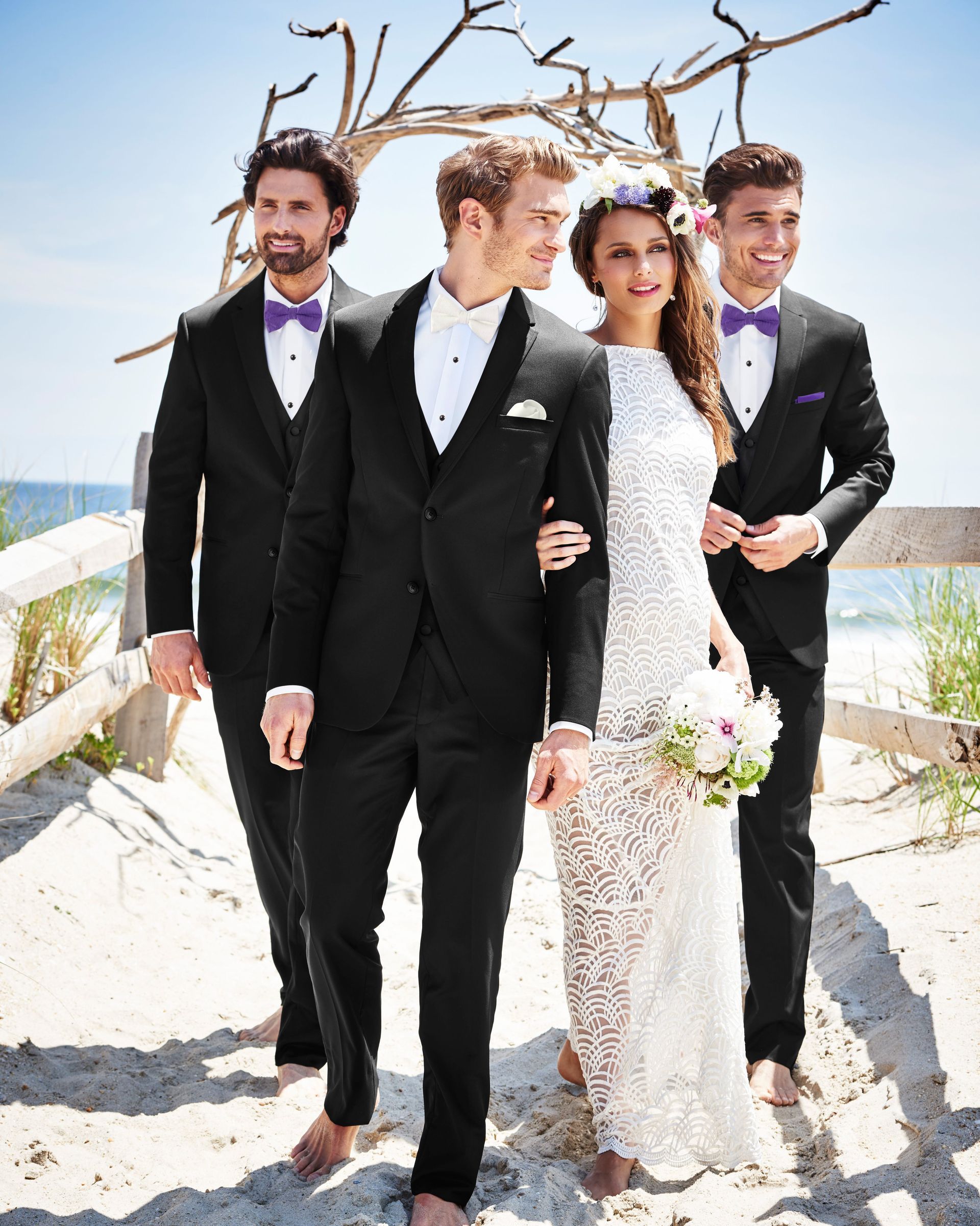 A bride and her groomsmen are walking barefoot on the beach.