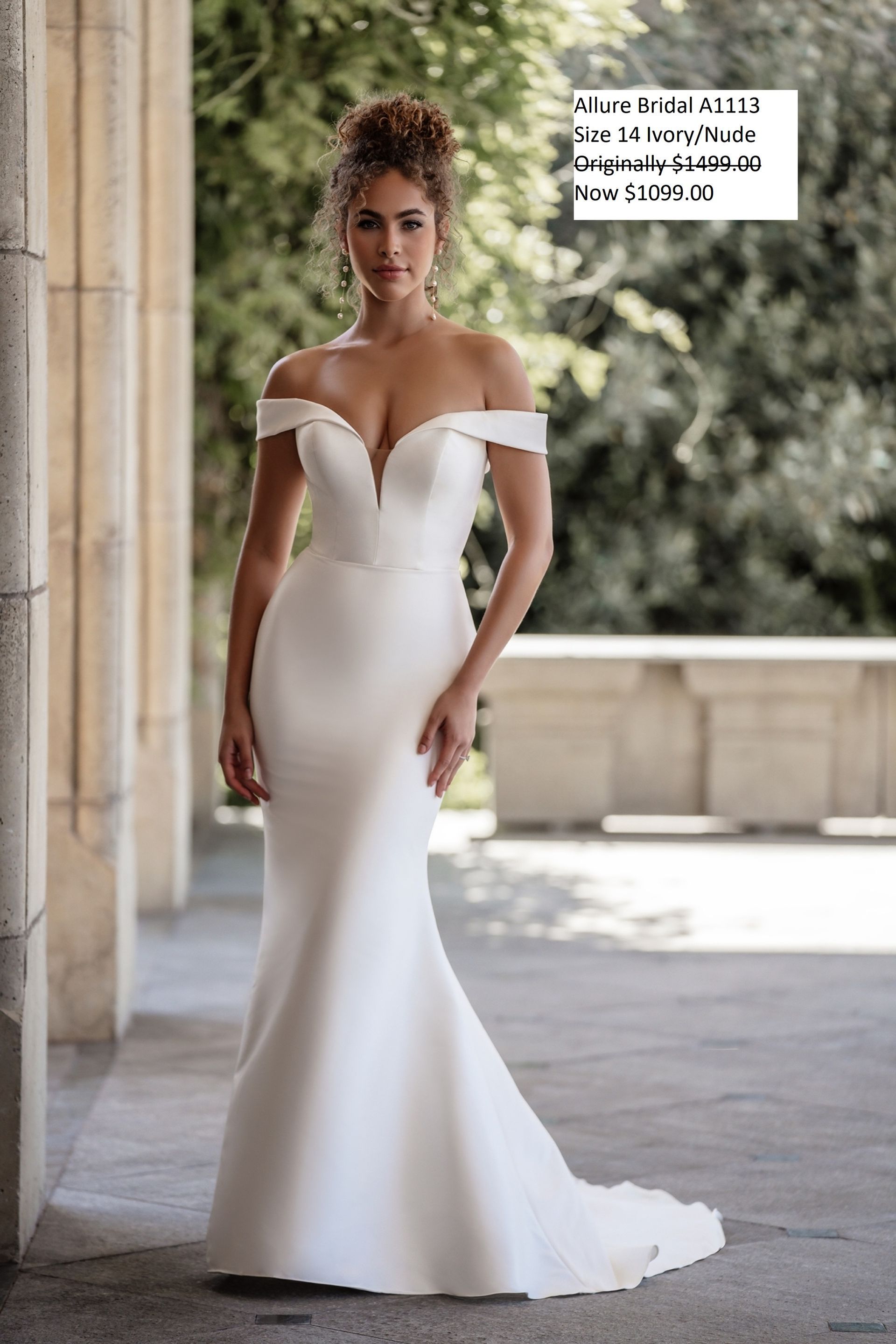 A woman is wearing a white off the shoulder wedding dress. Allure Bridal A1113