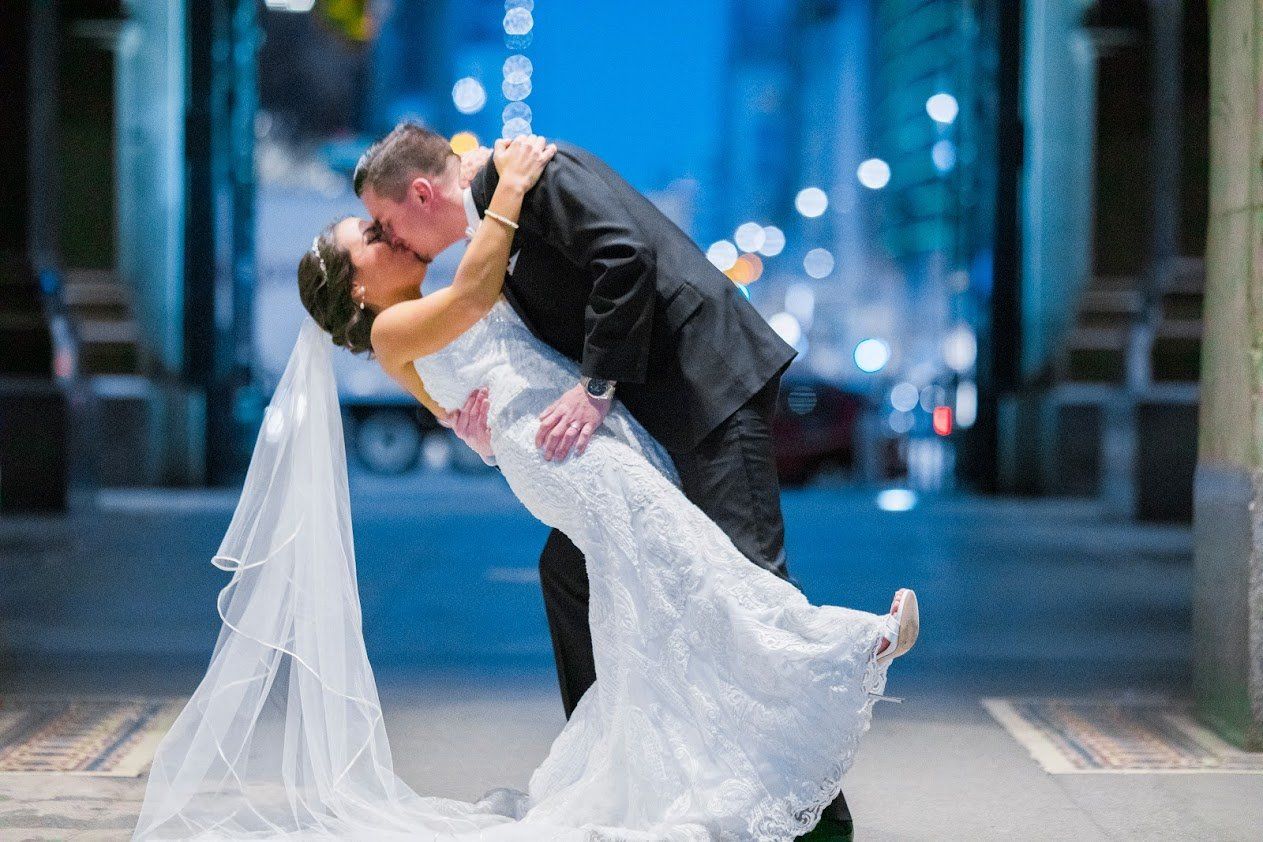 A bride and groom are kissing on a city street at night.