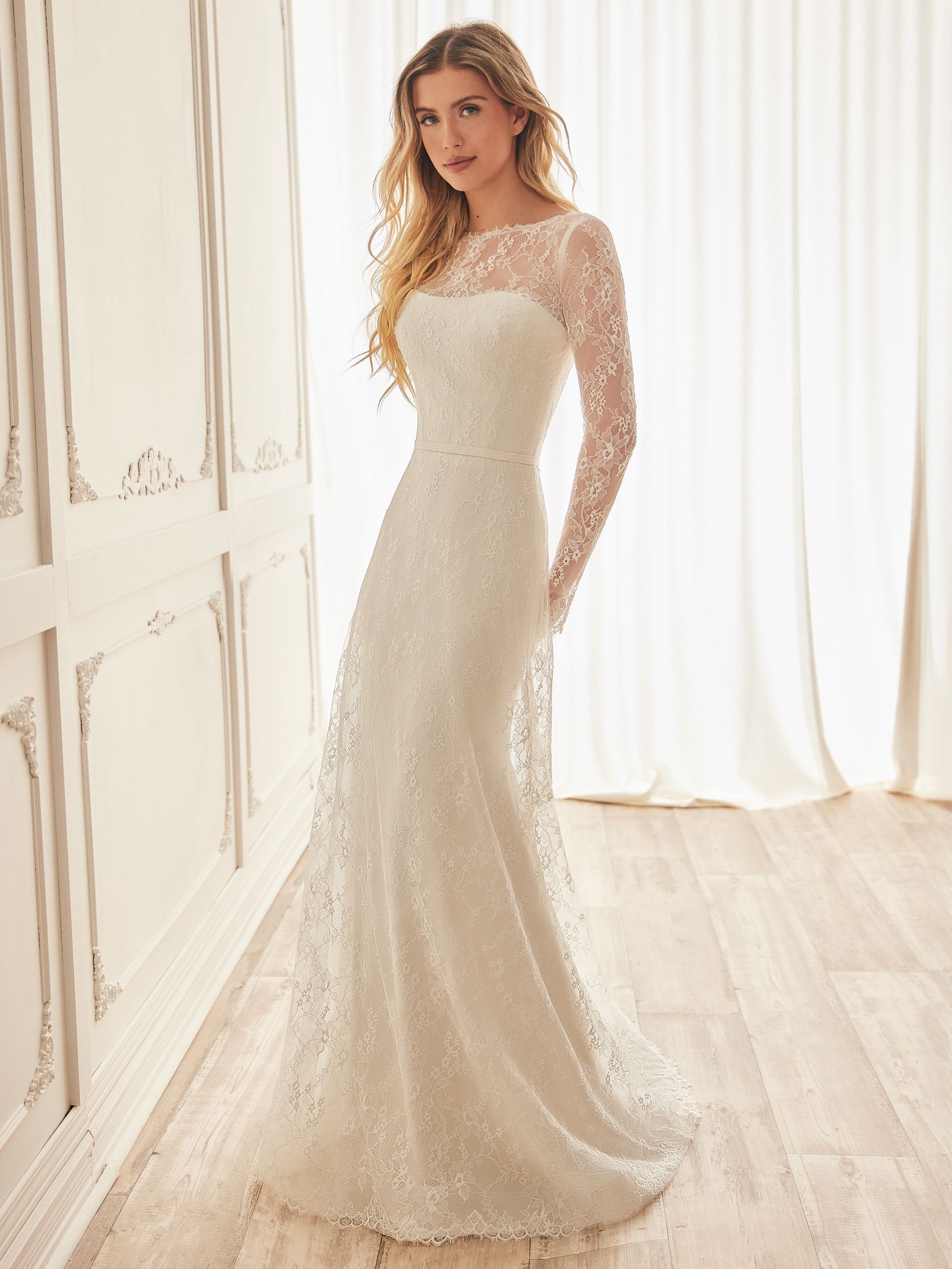 Woman in white lace wedding dress, standing indoors.