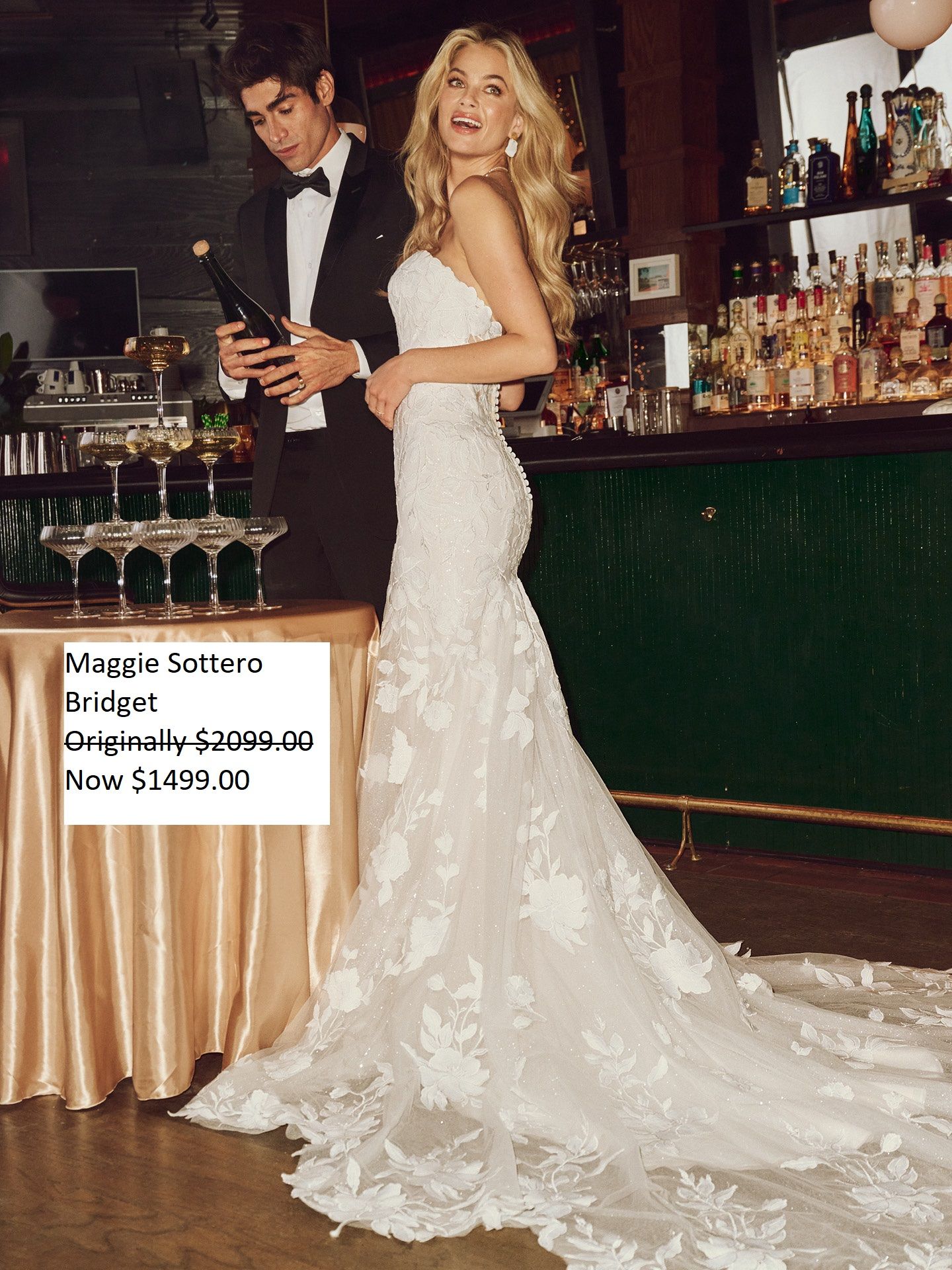 A couple at a bar, woman in a wedding dress. Man is pouring champagne. Price tag shown in front. Maggie Sottero Bridget