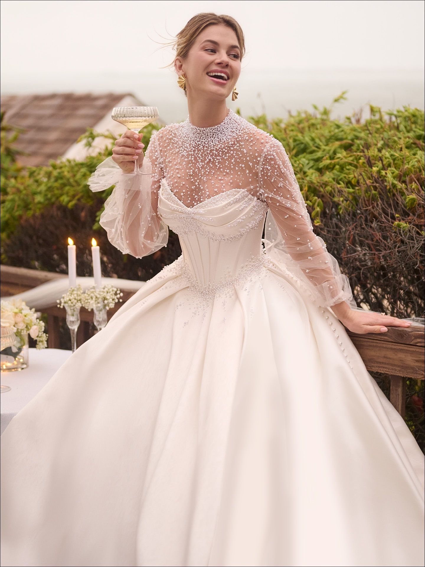 Woman in a white wedding gown, holding a drink, smiling, outdoors.